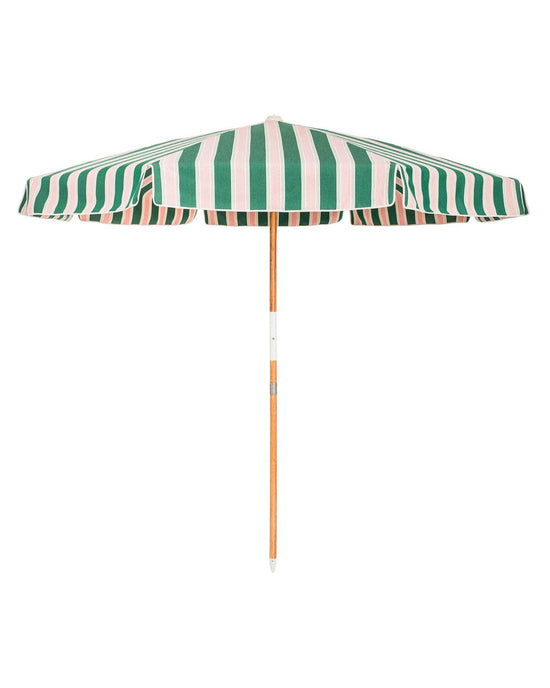 The Amalfi Umbrella - Bistro Green Stripe by Business & Pleasure Co is a Mediterranean-style beach umbrella with green and white stripes, a wooden pole, and UV protection, shown fully opened against a white background.