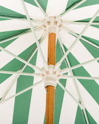 Close-up view from underneath the UV-resistant canopy of the Business & Pleasure Co Amalfi Umbrella - Crew Canyon Green Stripe, showing its wooden pole, white plastic hub, and spokes radiating outward.