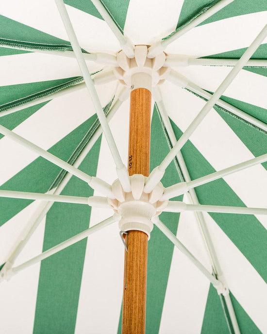 Close-up view from underneath the UV-resistant canopy of the Business & Pleasure Co Amalfi Umbrella - Crew Canyon Green Stripe, showing its wooden pole, white plastic hub, and spokes radiating outward.