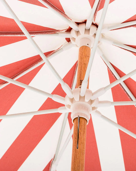 Close-up view from underneath the Amalfi Umbrella - Crew Le Sirenuse Stripe by Business & Pleasure Co, a red and white striped umbrella with a wooden pole, white spokes, and UV resistant fabric in a bold radial pattern.