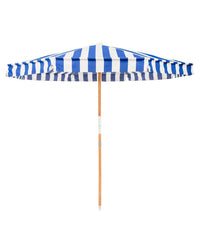 The Amalfi Umbrella - Crew Mediterranean Blue Stripe by Business & Pleasure Co features UV-resistant fabric, blue and white vertical stripes, and a wooden pole—perfect as a stylish Mediterranean beach umbrella for sunny days.