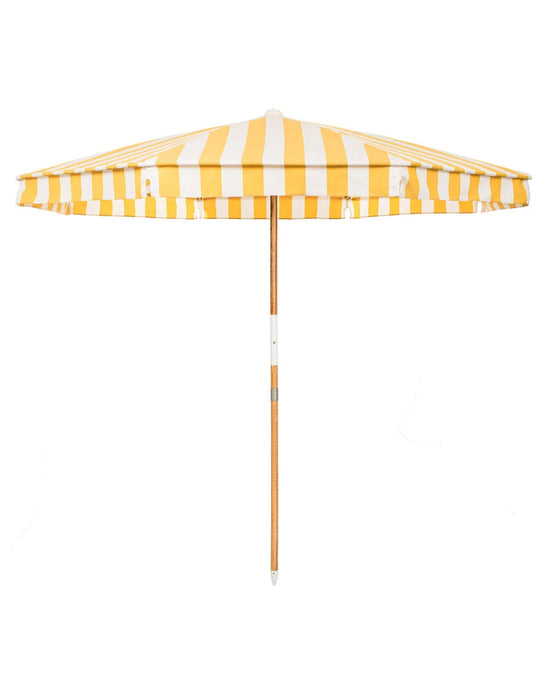 The Amalfi Umbrella - Crew Mimosa Yellow Stripe by Business & Pleasure Co features a yellow and white striped, UV-resistant canopy and a wooden pole, shown from the side against a plain white background.