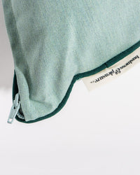 Close-up view of the Small Square Throw Pillow in Rivie Green by Business & Pleasure Co, crafted from Pleasuretex fabric, featuring a visible zipper and a partially exposed brand tag along the edge.
