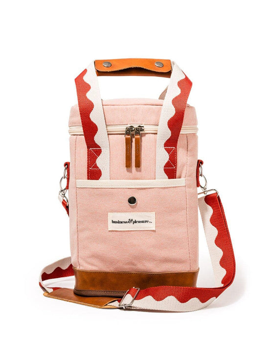 The Wine Cooler Tote Bag - Rivie Pink by Business & Pleasure Co features a pink insulated design with brown vegan leather accents, a white and red wavy shoulder strap, zipper closure, front pocket, and brand label.