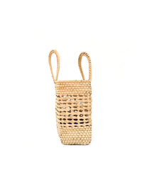 The Canasta Chica Bag in Natural by caminito is a handmade, beige basket-style bag with two handles, crafted from palm fronds and shown upright against a plain white background.
