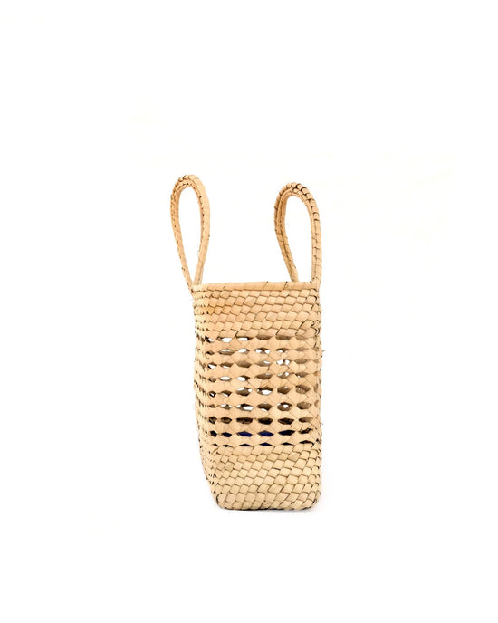 The Canasta Chica Bag in Natural by caminito is a handmade, beige basket-style bag with two handles, crafted from palm fronds and shown upright against a plain white background.