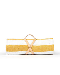 The caminito Marea Sol - Blanket Roll is a handwoven Mexican picnic blanket with wide yellow and white stripes, secured by a tan leather strap with handle, displayed on a plain white background.
