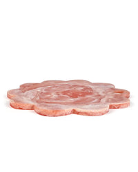 A side view of Casa Amarosas 12in Scallop Resin Cheese/Charcuterie Board in Pink shows its flower-inspired shape and marbled texture against a white background.