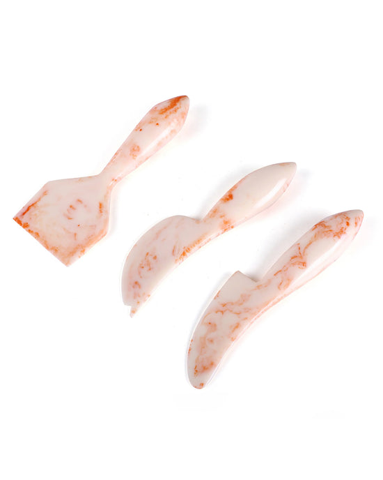 The Casa Amarosa Resin Cheese Knife Set of 3 in Ivory Pink features a spatula, spreader, and knife with a marble pattern, stylishly arranged on a white background.