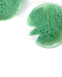 Two green, round objects with a marbled texture and a triangular notch rest on a white surface, echoing the unique design of Casa Amarosa’s Resin Short Salad Server Set in Green.