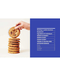 A hand places a chocolate chip cookie atop a stack of cookies next to a blue table of contents page from Cookies & Crumbs by Chronicle Books, featuring delicious cookie recipes.
