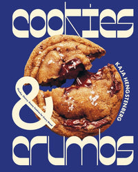 A large chocolate chip cookie broken in half sits on a blue background, with Cookies & Crumbs and Chronicle Books in white text, suggesting irresistible homemade cookie recipes.