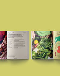Two open cookbooks on a yellow surface; the left shows salad recipes and a bowl of salad, while the right displays fresh veggies and vibrant art—perfect for any fan of Epic Salads by Chronicle Books.