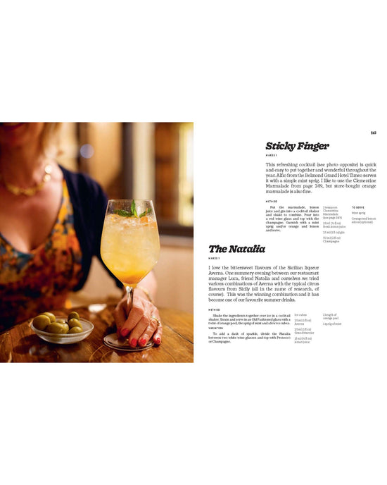 A woman enjoys a light orange cocktail with ice and mint next to green olives. On the right, Recipes from Sicily by Chronicle Books showcases cocktail ideas and classic Sicilian recipes from an authentic cookbook.