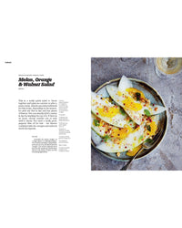 A bowl of melon slices with orange, walnuts, herbs, and seasoning—flavors inspired by Recipes from Sicily from Chronicle Books—served with a fork and a glass of white wine.