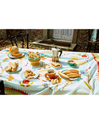 A table outdoors is set with bread, Sicilian pastries, coffee, and a moka pot, inspired by Sicily, My Sweet from Chronicle Books; a stone building and door can be seen in the background.