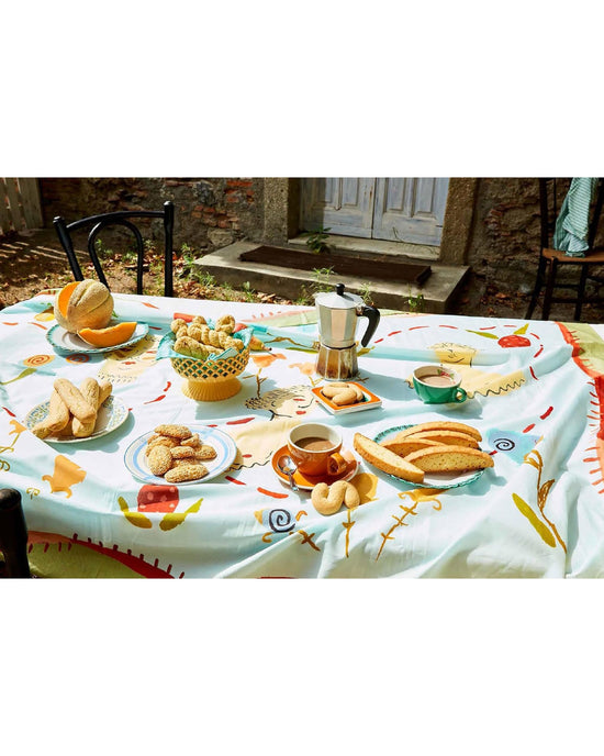 A table outdoors is set with bread, Sicilian pastries, coffee, and a moka pot, inspired by Sicily, My Sweet from Chronicle Books; a stone building and door can be seen in the background.