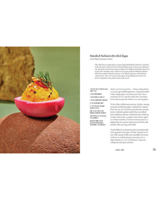 A halved pink deviled egg with smoked salmon filling, dill, and roe sits on a brown surface. Inspired by tinned fish recipes from Tin to Table by Chronicle Books, the recipe text is shown on the right.