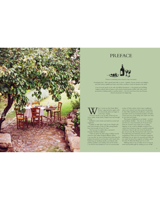 A rustic outdoor dining set sits on a stone patio beneath a leafy tree, beside Chronicle Books’ “Wild Figs and Fennel,” Letitia Clark’s Mediterranean cookbook with Italian recipes illustrated with wine, cheese, and grapes.