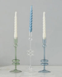The Clear Glass Candlesticks Set of 2 - Large by etúHOME are handcrafted from recycled glass, displayed here with blue and white spiral candles on a marble surface for a striking presentation.