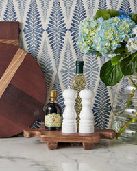 The etúHOME Normandy Wood Riser Footed Tray, Small, showcases a vinegar bottle, wine bottle, salt and pepper shakers, and a glass vase with blue hydrangeas on a marble counter set against blue leaf-patterned wallpaper.
