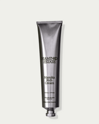 A metallic tube of Flamingo Estate’s Manuka Rich Cream stands upright against a plain light background, featuring black product details and a twist cap at the bottom.