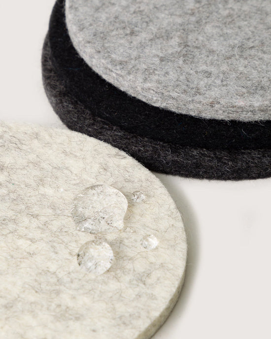 Close-up of three graf lantz Bierfilzl Merino Wool Felt Round Coasters Multi in Noir (4 Pack) in light and dark gray, with water droplets on the front—an elegant, sustainable addition to your home decor.