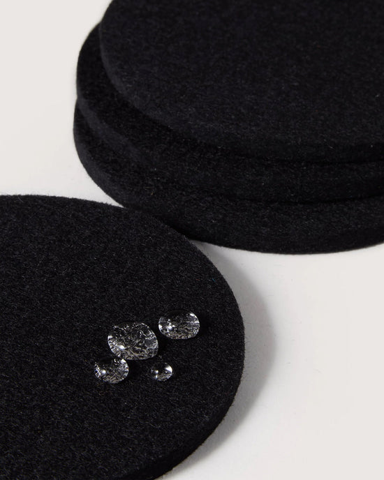 The graf lantz Bierfilzl Merino Wool Felt Round Coaster Solid in Black (4 Pack) adds an elegant, sustainable touch to your décor, shown here on a white surface with water droplets highlighting its absorbent design.