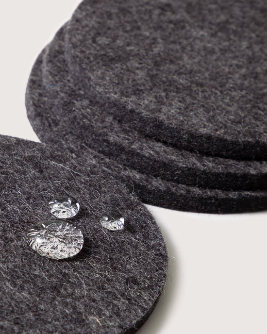 Four round charcoal Bierfilzl Merino Wool Felt Coasters by graf lantz are stacked, with three clear water droplets on the top—an elegant, sustainable touch for your home decor.