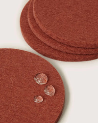 Four terracotta Bierfilzl Merino Wool Round Coasters by graf lantz are stacked on a white surface, with water droplets on one coaster—an elegant and sustainable touch for your home. Set includes 4 coasters.