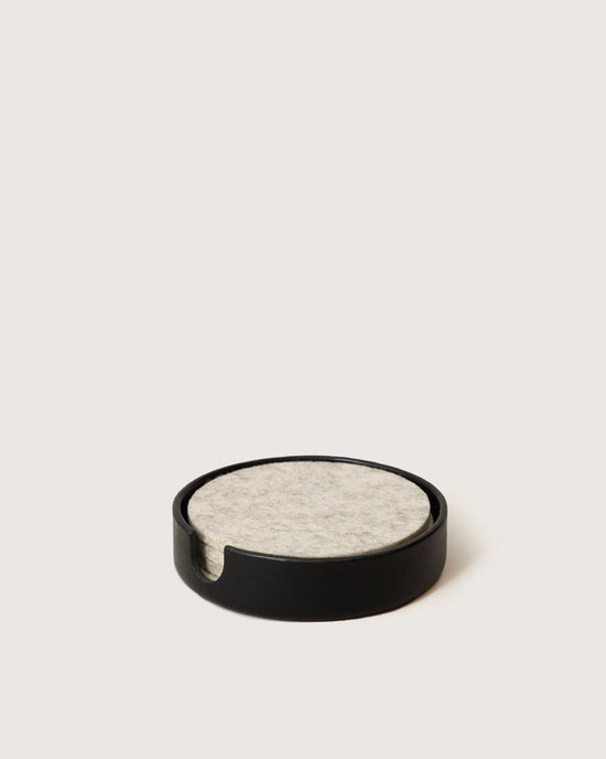 A stack of light grey felt coasters rests in the graf lantz Kobon Leather Round Tray in Black, which doubles as a sleek holder and stylish catch-all on a plain light surface.