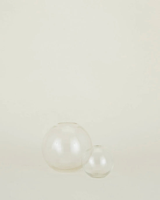 Two clear Aurora Sphere Vases by Hawkins New York, crafted from recycled handblown glass in different sizes, are arranged side by side on a plain, light background.
