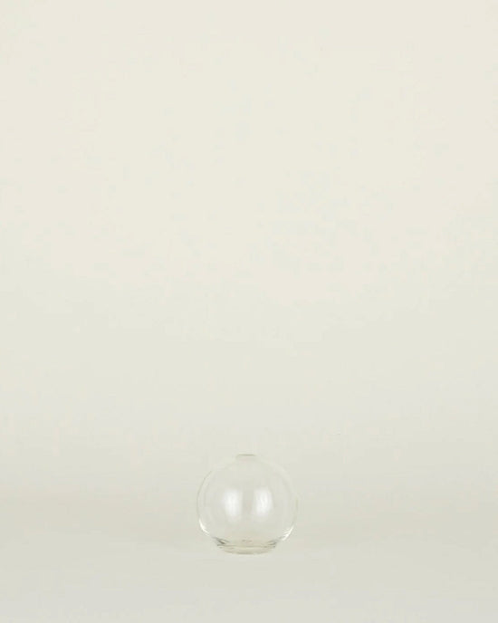 The Aurora Sphere Vase in Clear by Hawkins New York, crafted from recycled handblown glass, sits centered on a light surface with a neutral background.