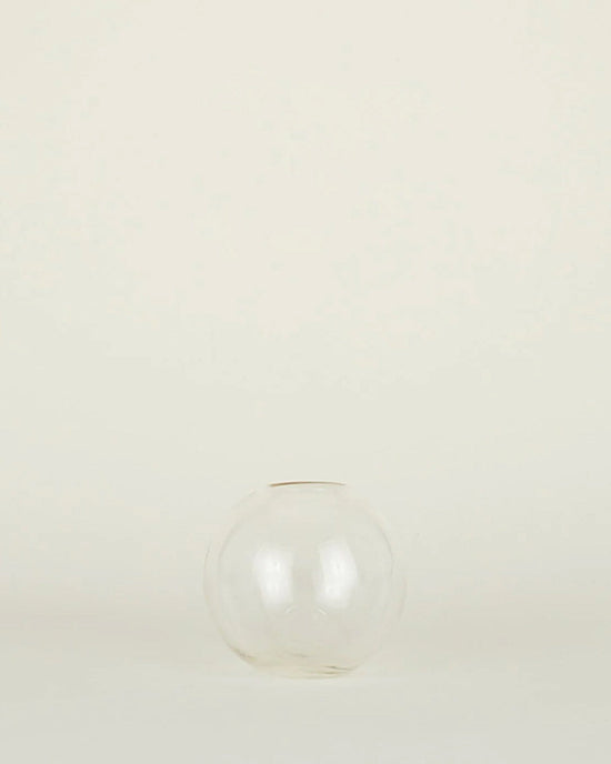 The Aurora Sphere Vase in Clear by Hawkins New York, crafted from recycled handblown glass, sits centered empty on a plain light background.