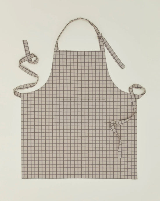 The Hawkins New York Essential Check Apron in Light Grey/Dark Grey features a chic check pattern, neck loop, and long waist ties—an elegant kitchen accessory, shown laid flat on a light background.