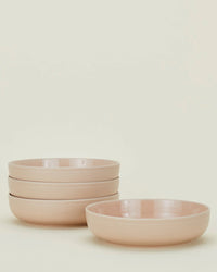 Four blush pink ceramic bowls from the Hawkins New York Essential Dinnerware 16 Piece Set are stacked, with one in front, against a plain off-white background.