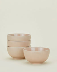 Four blush Essential Dinnerware bowls from Hawkins New York, three stacked and one in front on an off-white background—stylish, everyday dishwasher-safe pieces from their 16-piece set.