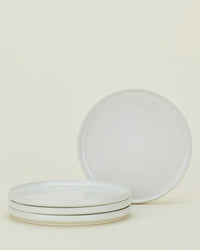 Four bone-colored ceramic plates from the Hawkins New York Essential Dinnerware 16 Piece Set are displayed—three stacked, one upright—against a light background, making them an ideal choice for any table.