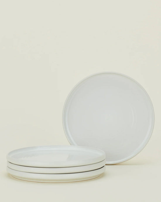 Four bone-colored ceramic plates from the Hawkins New York Essential Dinnerware 16 Piece Set are displayed—three stacked, one upright—against a light background, making them an ideal choice for any table.