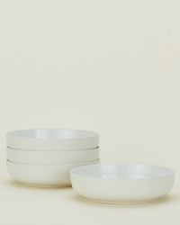 Four bone-colored ceramic bowls from the Hawkins New York Essential Dinnerware 16 Piece Set are shown, with three stacked on the left and one placed separately on the right against a plain light background.