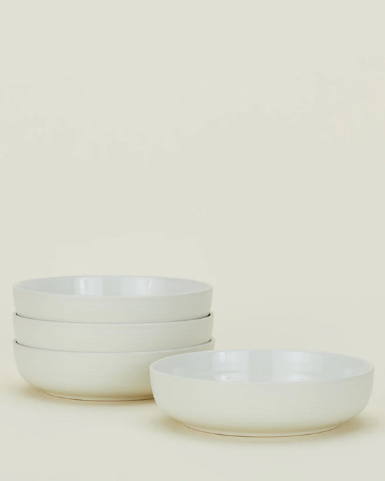 Four bone-colored ceramic bowls from the Hawkins New York Essential Dinnerware 16 Piece Set are shown, with three stacked on the left and one placed separately on the right against a plain light background.