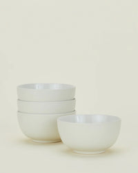 Four white ceramic bowls from the Hawkins New York Essential Dinnerware in Bone – 16 Piece Set, with three stacked on the left and one placed separately on the right, set against a plain light background.