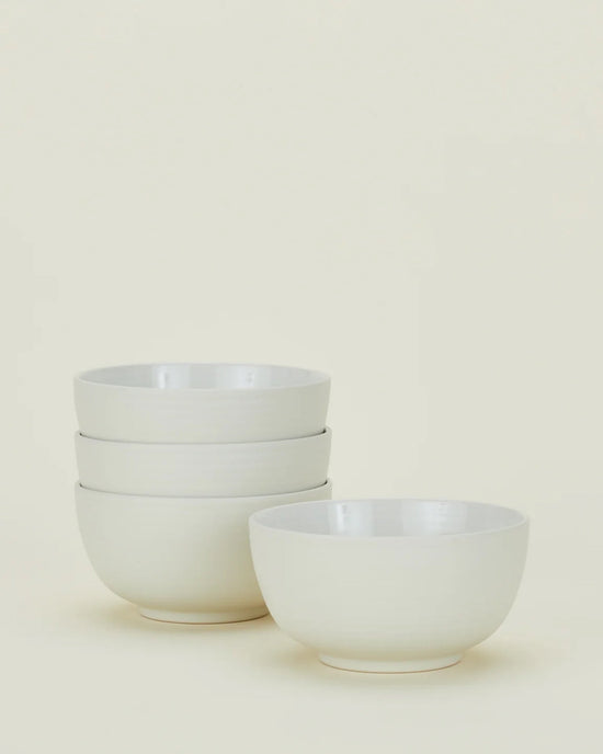 Four white ceramic bowls from the Hawkins New York Essential Dinnerware in Bone – 16 Piece Set, with three stacked on the left and one placed separately on the right, set against a plain light background.