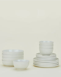 A set of stacked white ceramic bowls and plates from the Hawkins New York Essential Dinnerware in Bone 16 Piece Set is arranged neatly against a plain light background.