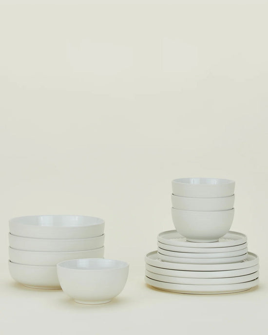 A set of stacked white ceramic bowls and plates from the Hawkins New York Essential Dinnerware in Bone 16 Piece Set is arranged neatly against a plain light background.