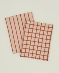 Two folded Hawkins New York Essential Dish Towels in Blush/Terracotta, one with vertical brown stripes and the other with a brown checkered pattern, made of Oeko-Tex cotton, are displayed on a plain light background.
