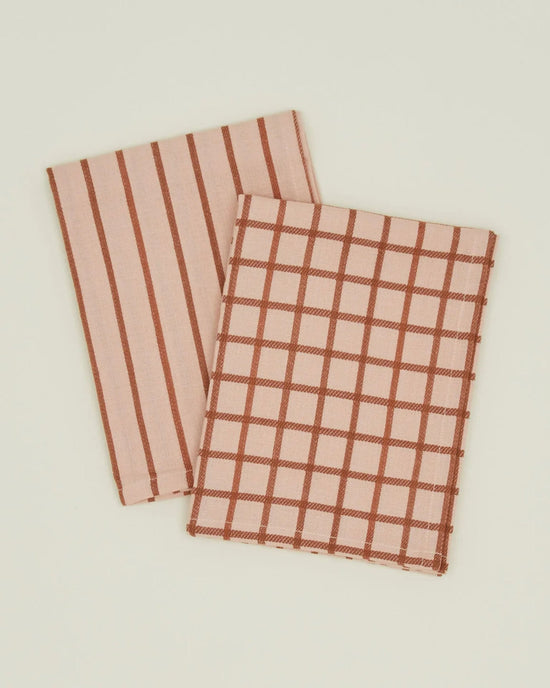 Two folded Hawkins New York Essential Dish Towels in Blush/Terracotta, one with vertical brown stripes and the other with a brown checkered pattern, made of Oeko-Tex cotton, are displayed on a plain light background.