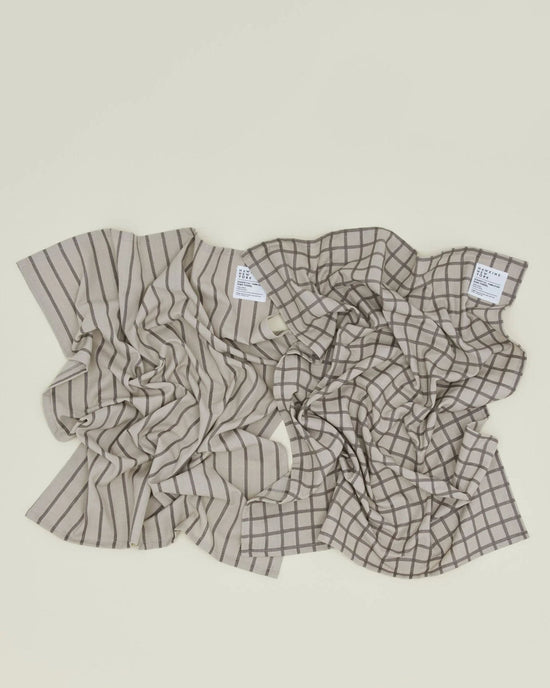 A set of two Hawkins New York Essential Dish Towels in Light Grey/Black—one striped, one checkered—lies side by side on a light surface.