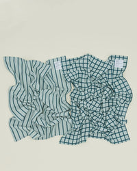 Two Essential Dish Towels in Sky/Peacock by Hawkins New York—one striped, one grid patterned—are placed side by side on a light-colored surface.