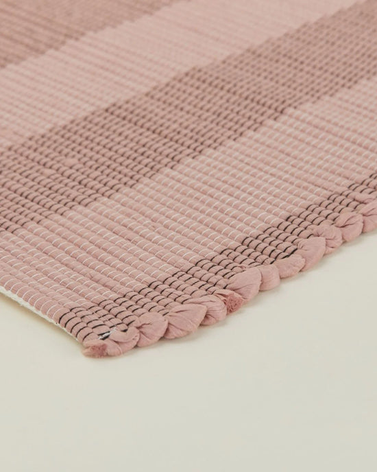 Close-up of the Hawkins New York Essential Floor Mat in Blush, featuring pink and beige stripes with braided edge detailing, displayed on a light-colored surface.
